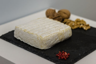 Tomino cheese on black tablecloth decorated with small red berries and walnuts.