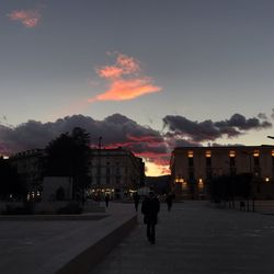 Silhouette people on illuminated street against sky at sunset