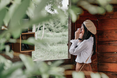 Woman holding mobile phone while standing on wood