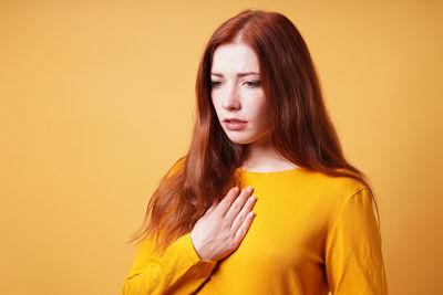 Young woman standing against yellow background