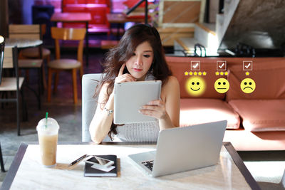 Portrait of young woman using phone while sitting on table