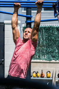 Muscular male athlete in sportswear doing exercises on monkey bar while practicing endurance during training on sports ground