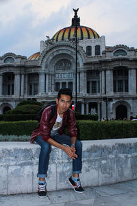 Portrait of man sitting on retaining wall against palacio de bellas artes