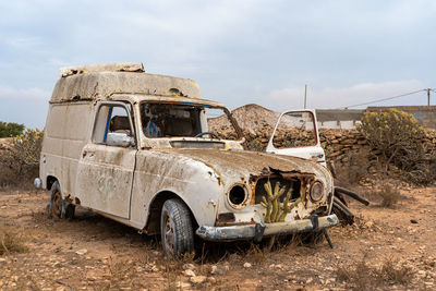 Old abandoned car on land against sky