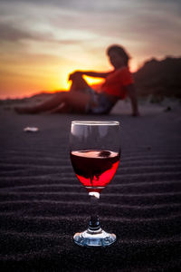 Man and wine in glass against sky during sunset