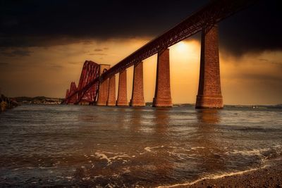 Low angle view of bridge over sea during sunset