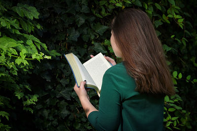 Rear view of woman reading book against plants