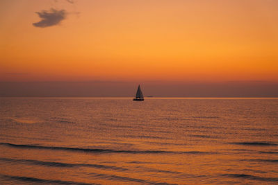 Silhouette sailboat in sea against orange sky