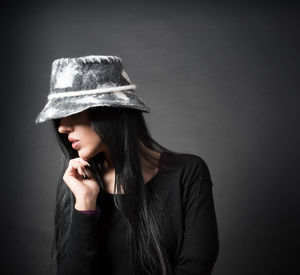 Portrait of beautiful young woman wearing hat against black background