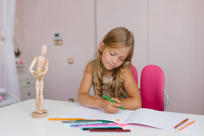 Seven year old schoolgirl is doing homework at her desk at home or at school, drawing