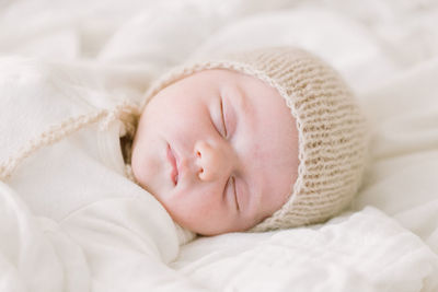 Newborn baby in knit bonnet sleeping on white bed