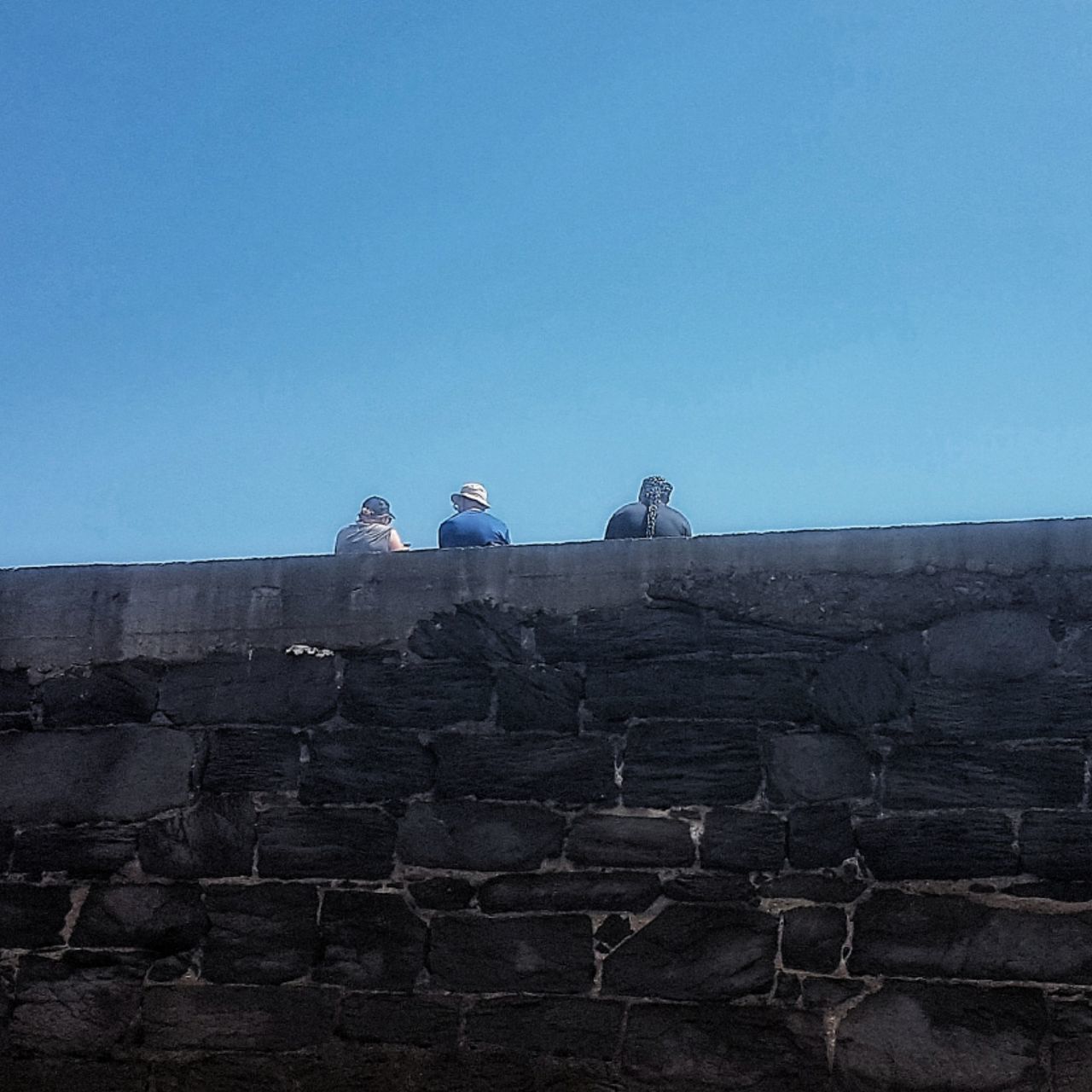 LOW ANGLE VIEW OF PEOPLE STANDING ON COBBLESTONE AGAINST CLEAR SKY