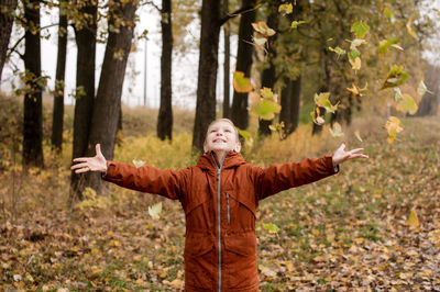 The boy tossed autumn yellow leaves and looks up