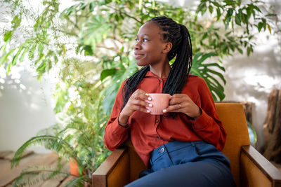 Portrait of young woman using mobile phone while sitting against plants