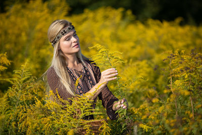Portrait of young woman standing amidst yellow flowering plants on field