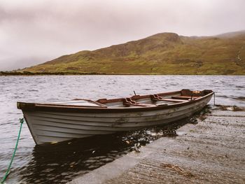 Boat moored on shore by lake against sky