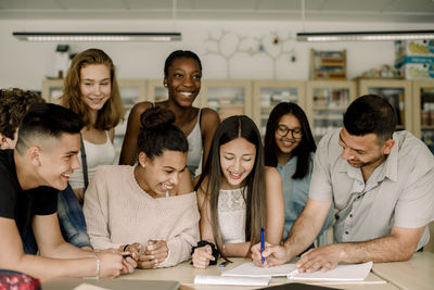 Smiling tutor teaching male and female students while leaning over table in classroom