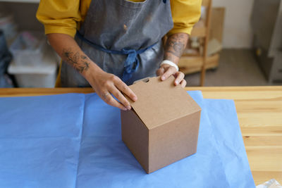 Woman self-employed ceramist packing carton box with handmade crockery to deliver parcel to customer