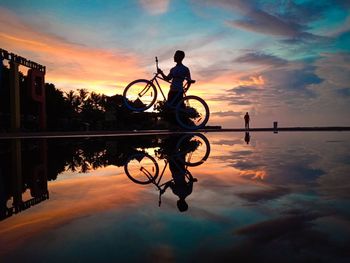 Silhouette bicycle by lake against sky during sunset
