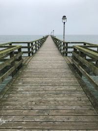 Wooden footbridge on pier over sea against sky