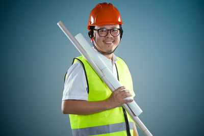 Portrait of smiling construction worker standing against colored background