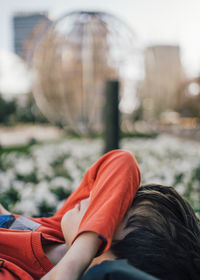 Side view of young boy lying in a city street park ground hiding face under arm covering eyes