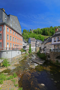 Buildings by river against blue sky