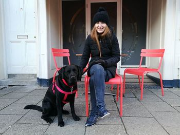 Portrait of smiling mature woman by dog sitting on chair at sidewalk