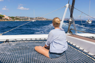 Rear view of man sitting on sailboat in sea against sky
