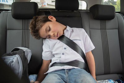 Toddler boy sleeps peacefully and safe while secured with seat belts in the car