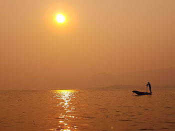 Silhouette man in sea against sky during sunset