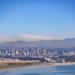 View of city and mountains at waterfront against blue sky