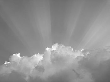 Low angle view of sunlight streaming through clouds