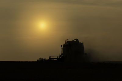 Silhouette factory on field against sky during sunset