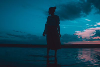 Rear view of silhouette man standing by swimming pool against sky