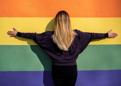 Rear view of woman with arms outstretched standing against colorful wall