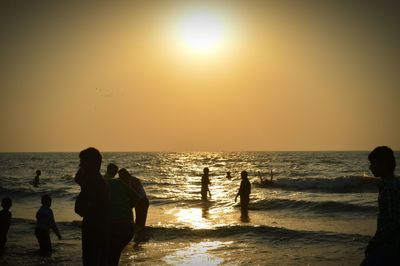 Silhouette people on beach against sky during sunset