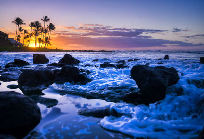 Rocks on sea shore against sky during sunset