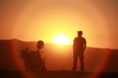 Rear view of silhouette man riding motorcycle against orange sky