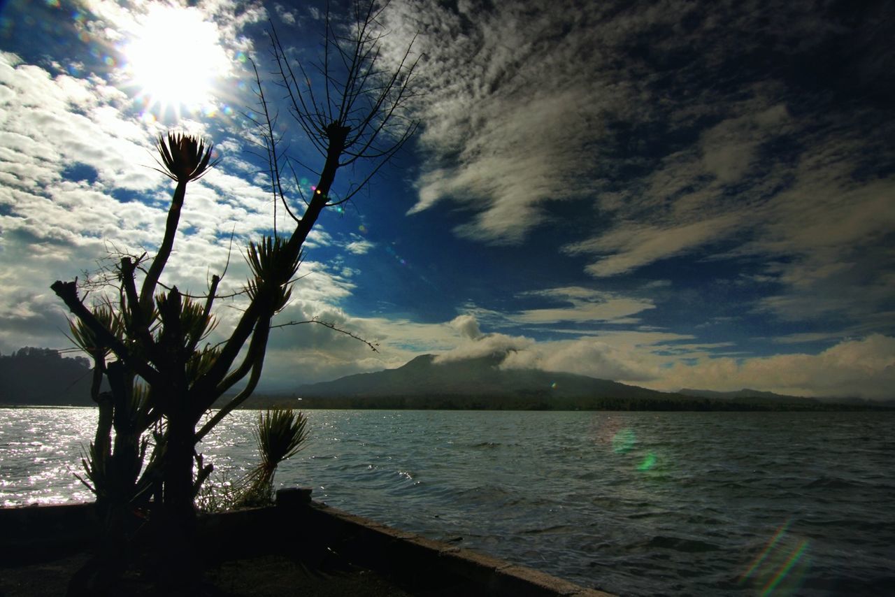 water, sky, tranquil scene, sea, tranquility, scenics, beauty in nature, cloud - sky, nature, silhouette, sun, horizon over water, cloud, mountain, tree, cloudy, sunlight, idyllic, rippled, lake