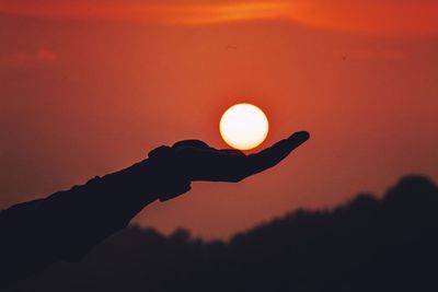 Optical illusion of silhouette hand holding sun during sunset