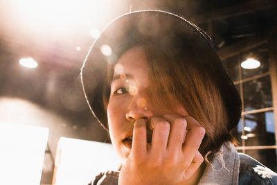 Close-up portrait of young woman wearing hat in illuminated room