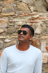 Young man wearing sunglasses standing against stone wall