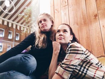 Low angle view of female friends by wooden wall