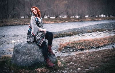 Woman sitting on rock at shore during winter