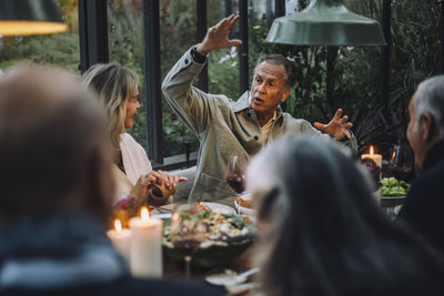 Senior man gesturing while talking to friends during dinner party