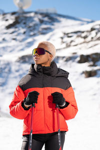 Una mujer afroamericana con bastones de esquí de pie en una montaña nevada durante el invierno