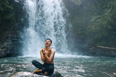 Full length of man sitting on rock in forest