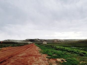 Empty road amidst field against sky