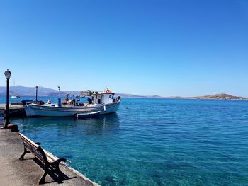 Boats moored on sea against clear blue sky